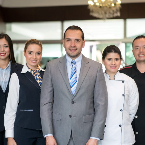 Portrait of hotel staff group including manager, receptionist, chef and bellboy looking at the camera smiling
