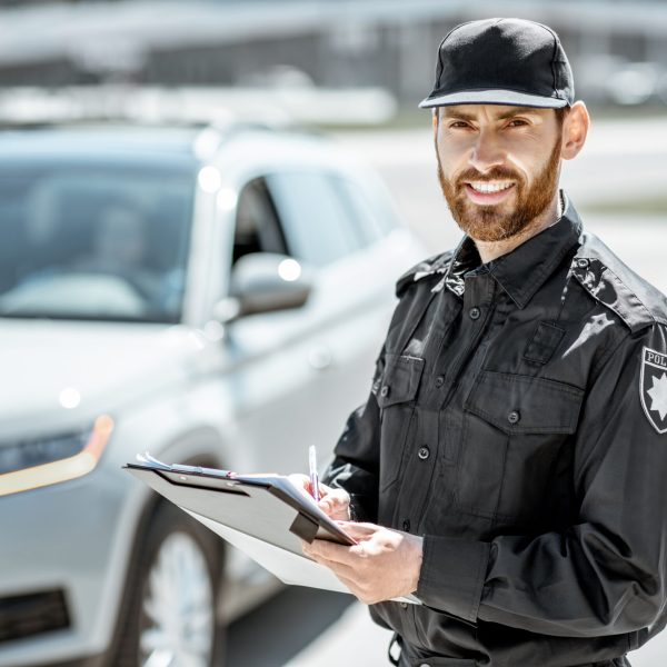 Portrait of a handsome policeman in uniform standing in front of a car on the roadside
